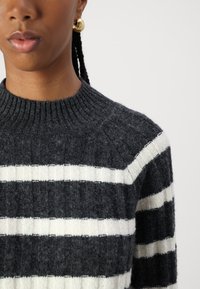 Pull en laine tricoté avec des larges rayures gris foncé et blanches, un col côtelé et un tissu texturé au toucher doux.