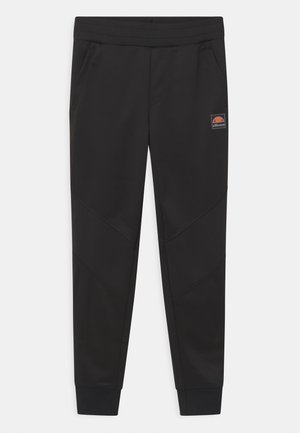 Pantalon de jogging noir fuselé avec des panneaux côtelés aux genoux, taille élastique et poignets, poches latérales, et un petit patch logo Ellesse sur la cuisse.