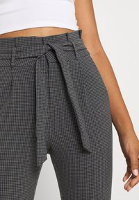Pantalons à carreaux gris et marine avec un détail de taille nouée, présentant un tissu texturé et une coupe ajustée.