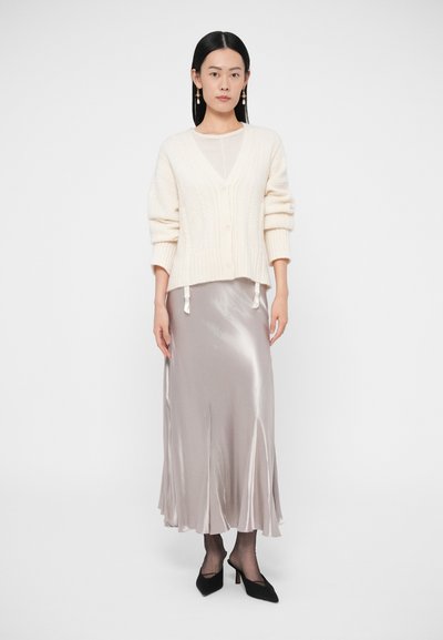 Krém színű kötött kardigán fonott mintával, selymes, világosszürke, bokáig érő szoknyával párosítva. A megjelenést fekete, hegyes orrú magassarkú cipő teszi teljessé.