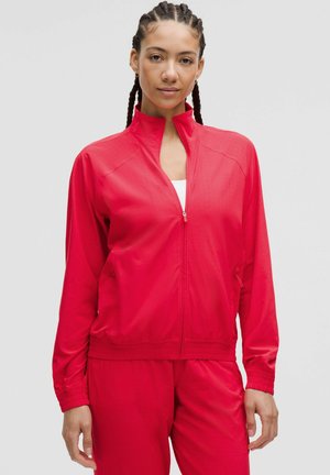Röd zip-up sportjacka i ett smidigt, lätt material. Har en stående krage, sidofickor och elastiska muddar.