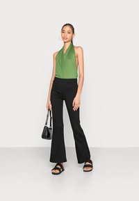Top halter verde e calças pretas flare, com uma textura suave e elástica. Acessorizado com uma pequena bolsa preta e sandálias com plataforma.