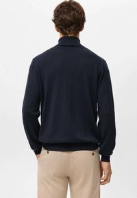 Marineblauwe trui met hoge kraag, lange mouwen en geribde boorden, van achteren getoond, met een zachte textuur.