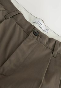 Barna, laza, keskenyedő szabású nadrág gombos záródással, övbújtatókkal és egy fehér, "NEXT" feliratú belső derékpánttal.