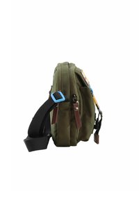 Borsa a tracolla verde in tela con una sola cintura, caratterizzata da un accento in hardware blu, dettagli con toppe e due scomparti con zip.