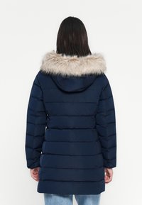 Cappotto puffer blu navy con cappuccio foderato in pelliccia sintetica, design trapuntato e taglio lungo fino al ginocchio. Presenta maniche lunghe e orlo dritto.