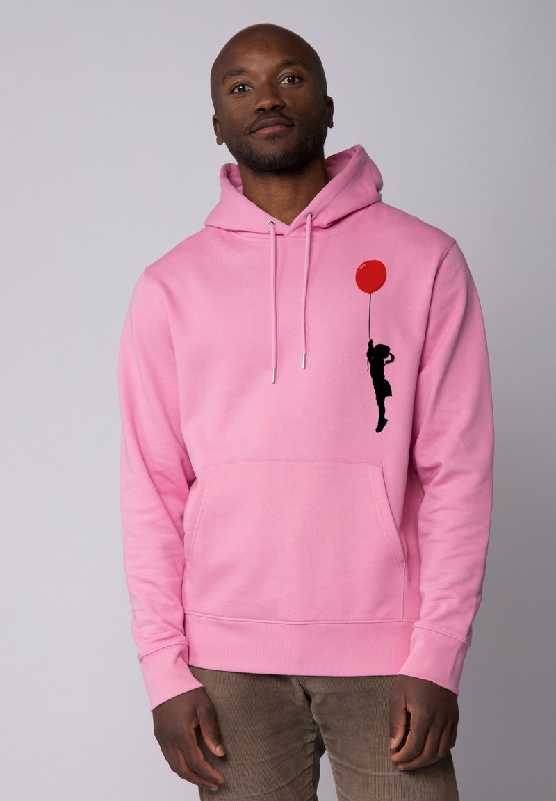 Roze hoodie met een voorzak, met een zwarte silhouet van een persoon die een rode ballon vasthoudt als grafisch detail. Zacht materiaal, lange mouwen.