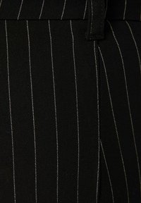 Svart tyg med vita vertikala ränder. Texturen verkar slät med en lätt lyster. Har en midjeband och sömnadsdetaljer.