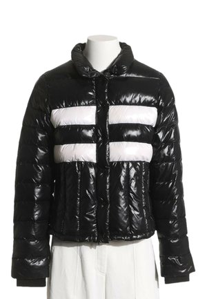 Chaqueta acolchada negra brillante con rayas horizontales blancas en el pecho, cremallera frontal, mangas largas y cuello alto en un maniquí blanco.