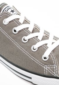 Gray canvas sneaker with white laces, silver eyelets, contrasting white stitching, and a black rubber sole with a white stripe.