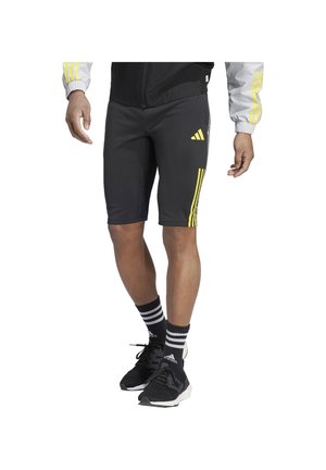 Schwarze Sportshorts mit gelbem Dreistreifen-Design, enganliegendem Schnitt und glatter Textur, kombiniert mit schwarzen Turnschuhen und gestreiften Socken.