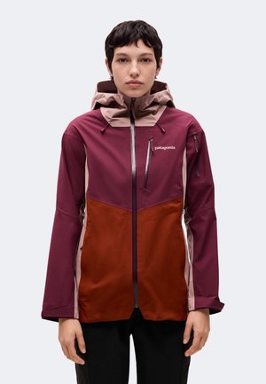 Un mannequin porte une veste d’extérieur Patagonia bordeaux et rouille, avec une capuche haute, une fermeture éclair sur le devant et des poches poitrine, sur un fond uni.