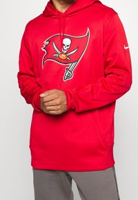 Sweat à capuche Nike rouge arborant le logo des Tampa Bay Buccaneers. Tissu doux, manches longues, capuche réglable avec cordon de serrage, coupe décontractée avec poches latérales.