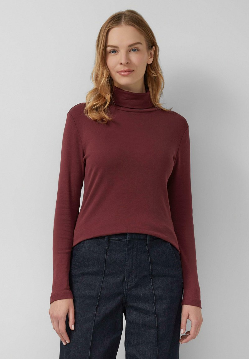 Bordeauxrode turtleneck top van rekbare stof, lange mouwen, aansluitend ontwerp, effen textuur, gecombineerd met donkere denim broek met verticale naden.