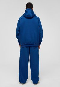 Blauwe joggingbroek en hooded sweatshirt van zachte stof. Het ontwerp heeft een losse pasvorm met rib gebreide boorden en een buidelzak.
