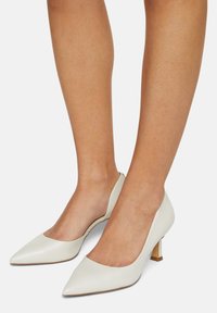 Valkoiset nahkaiset korkokengät, joissa on terävä kärki, matala lohkokorko ja leikattu muoto sivuilla. Silkkinen tekstuuri ja minimalistinen tyyli.