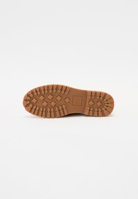 Semelle de chaussure en caoutchouc marron avec un design texturé et patterné comportant des grips triangulaires et hexagonaux pour l'adhérence. Logo carré au centre.