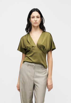Olivengrøn satinviklet top med dyb V-hals, korte ærmer og blød tekstur; kombineret med lysegrå bukser med nålestriber.