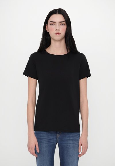 T-shirt noir à manches courtes avec un col rond, fabriqué en tissu lisse, associé à un jean bleu. Design simple et dépouillé sans motifs.