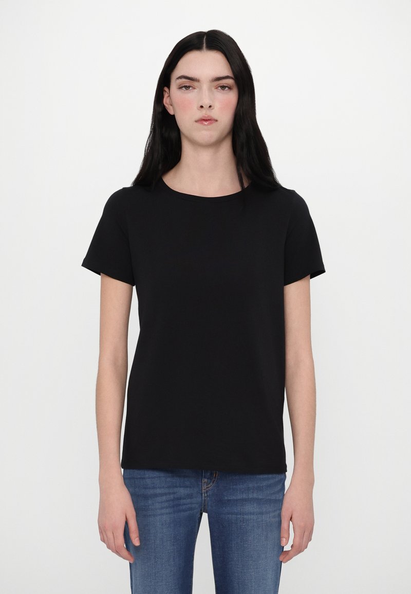 Sort T-shirt med korte ærmer og rund hals, lavet af glat stof, parret med blå jeans. Enkel, umasket design uden mønstre.