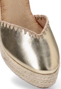 Espadrille metálica dorada con punta redondeada, plataforma de yute trenzado y un acento cosido alrededor del borde. Textura suave con acabado brillante.