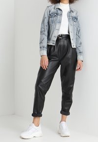 Ljus denimjacka med svarta grafiska mönster, vit stickad topp, hög midja svarta läderbyxor och vita sneakers.