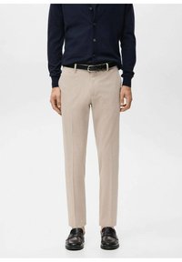Pantalones beige a medida con corte recto, tejido texturizado y pliegues delanteros, combinados con un cárdigan de botones azul marino y zapatos negros.