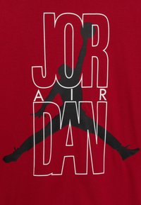 Red cotton t-shirt featuring bold black and white "JORDAN" text with a silhouette of a jumping figure in the center.