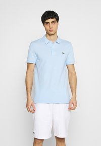 Polo shirt azzurro con maniche corte, patta a due bottoni e logo verde. Abbinato a pantaloni corti bianchi. Design semplice e texture in cotone.