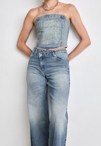 Top senza spalline in denim con decorazioni argentate, abbinato a jeans a gamba larga blu chiaro, entrambi con una finitura lavata e stile classico a cinque tasche.