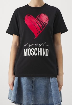 Sort t-shirt med stort rødt hjerte grafik og hvid tekst "40 år med kærlighed MOSCHINO", båret med en blå denim nederdel.