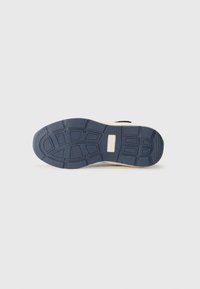 Sottopiede della sneaker realizzato in un materiale di gomma blu flessibile, con un motivo per il grip, accompagnato da una intersuola beige e un piccolo accento verde.