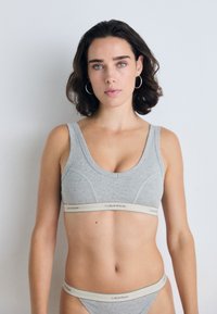 Pilkas medvilnės braletė ir derančios kelnaitės su plačia elastinga juosta, kurioje yra Calvin Klein logotipas natūralaus atspalvio. Prigludęs dizainas su lygiu paviršiumi.