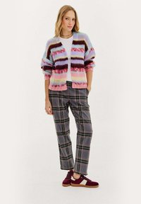 Szary kardigan w pastelowych paskach w odcieniach niebieskiego, różowego i bordowego, zestawiony z szarymi spodniami w kratę oraz burgundowymi sneakersami niskimi z białymi akcentami.