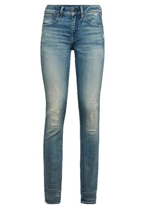 Jean slim bleu avec zones délavées et patchs usés sur les cuisses, doté de poches avant, passants de ceinture et fermeture à boutons.