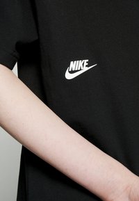 Mustat puuvillapaita, jossa on valkoinen Nike-logo painettuna vasemmalle puolelle. Kangas näyttää pehmeältä ja siinä on rento istuvuus.