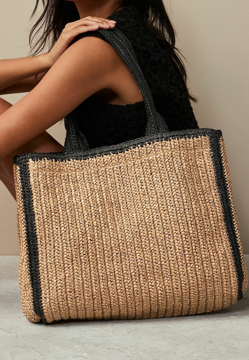 Geweven tan rieten tas met zwarte accentstrepen, voorzien van stevige handvatten en een gestructureerde afwerking, ideaal voor casual gebruik.