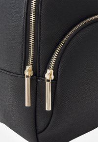 Zaino in faux pelle nera con superficie texturizzata, dotato di due cerniere dorate e tirazip metallici.