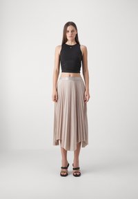 Top corto negro combinado con una falda plisada beige. La falda tiene una cinturilla suave y un diseño fluido en capas. Tacones negros con tiras.