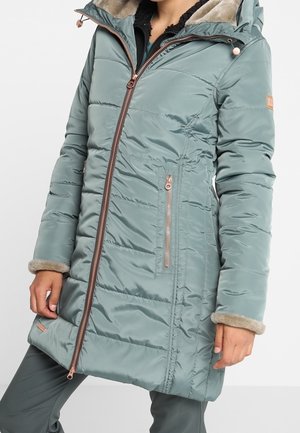 Mujer con abrigo de invierno largo acolchado de color azul claro, con capucha, cierre frontal de cremallera, bolsillos laterales con cremallera y ribete de piel beige en los puños y el forro de la capucha.