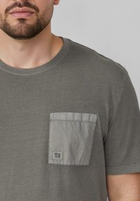 Szara koszulka z krótkim rękawem, z okrągłym dekoltem i kontrastową, płaską kieszonką. Wykonana z miękkiego materiału o gładkiej fakturze i subtelnych detalach szwów.