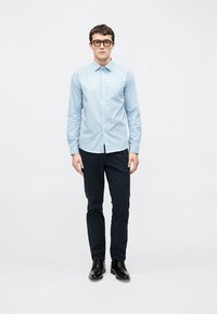 Lyseblå skjorte med knapper, krage og lange ermer, kombinert med mørkeblå bukser og svarte sko. Slim fit-design med subtilt mønster.
