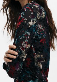 Black floral blouse with long sleeves, featuring a textured pattern in red, teal, and cream, and a subtle sheen.