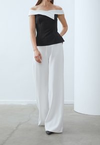 Černý a bílý top s odhalenými rameny ve stylu peplum, doplněný volnými bílými kalhotami. Hladká tkanina se strukturovaným siluetou. Černé špičaté podpatky.