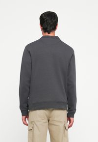 Sweatshirt gris foncé avec un col et des poignets côtelés, présentant une coupe décontractée et sans logos ni motifs visibles, associé à un pantalon cargo en kaki.