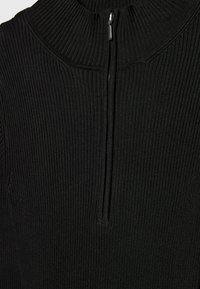 Pull noir côtelé avec col montant et fermeture éclair frontale. Tissu texturé avec des lignes verticales, mettant en valeur une silhouette ajustée.