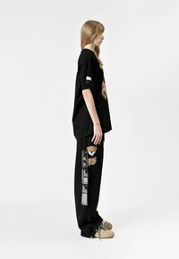 Camiseta negra de gran tamaño con un gráfico de oso, combinada con pantalones negros que tienen un parche de oso y detalles impresos a lo largo del costado.