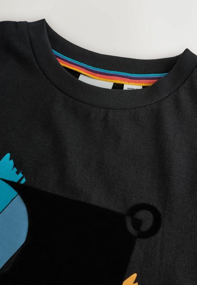 Musta puuvillapaita, jossa on värikäs graafinen kuvasto, jossa on sinisiä, keltaisia ja mustia elementtejä. Pyöreä kaula-aukko, jossa on monivärinen raidallinen vuori.