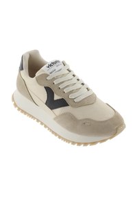 Baskets beiges et crème en cuir et daim, avec une semelle texturée, des lacets plats blancs et un accent de logo noir sur le côté.