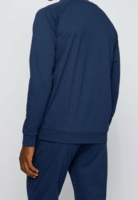Sudadera azul marino de manga larga con ribete en el dobladillo, hecha de una tela suave. Presenta un escote redondeado y un diseño sencillo.
